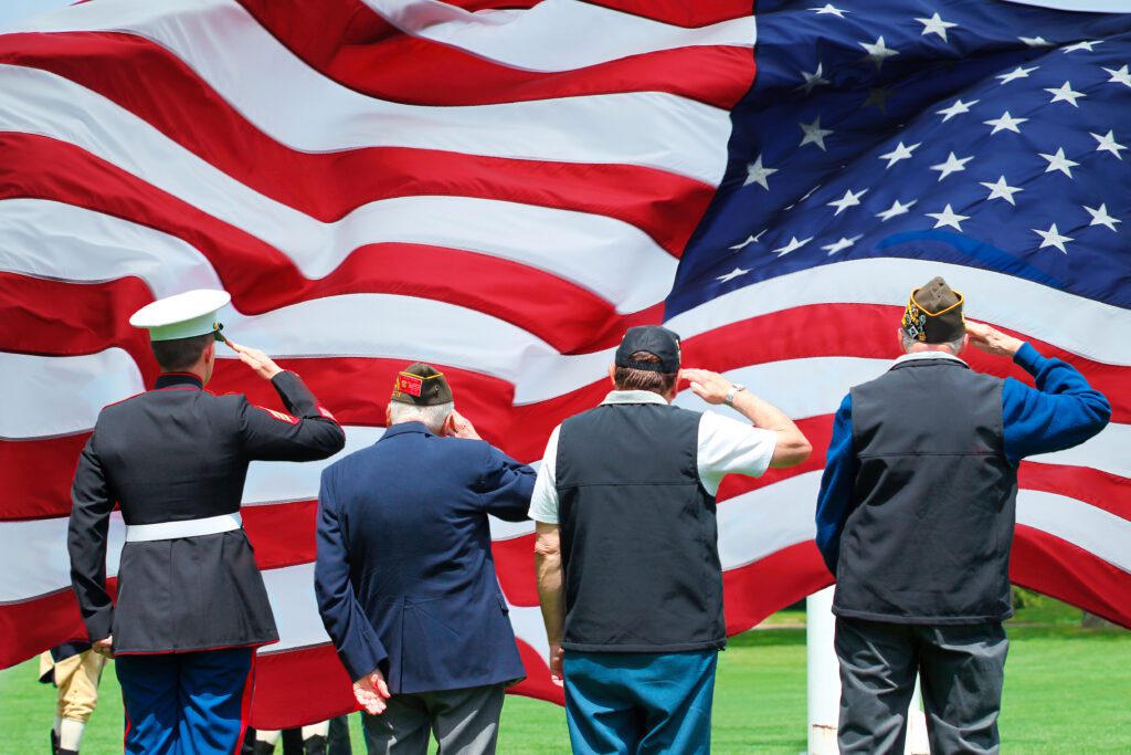 A marine and three veterans facing an American flag and saluting.